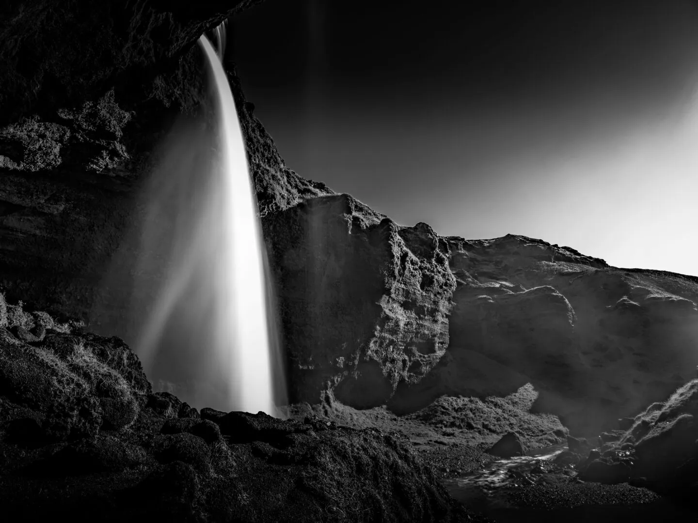 A waterfall pouring into a dark canyon, in black and white
